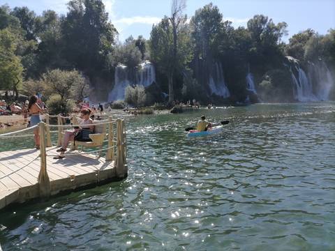       People kayaking and relaxing near a waterfall.
  