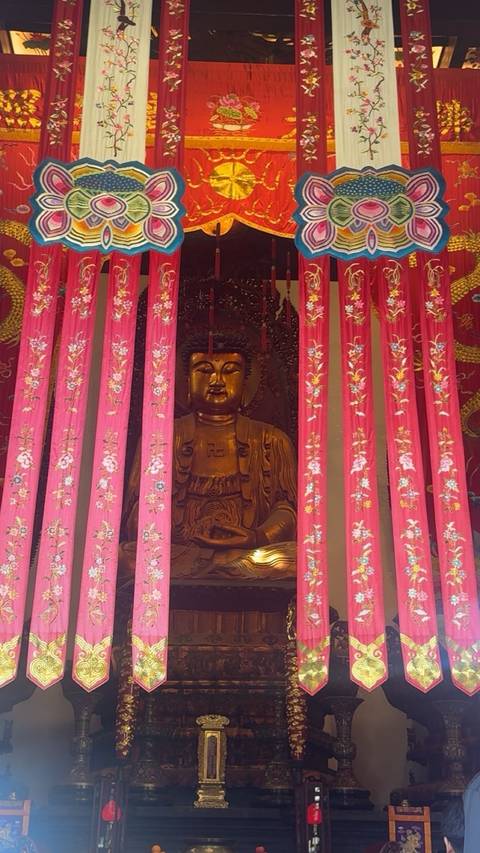       A golden Buddha statue behind red curtains.
  