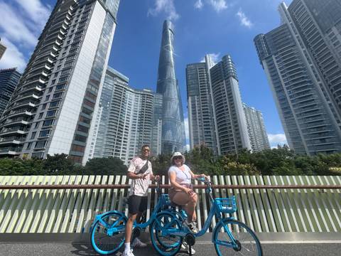       Two people on bicycles in front of modern skyscrapers.
  