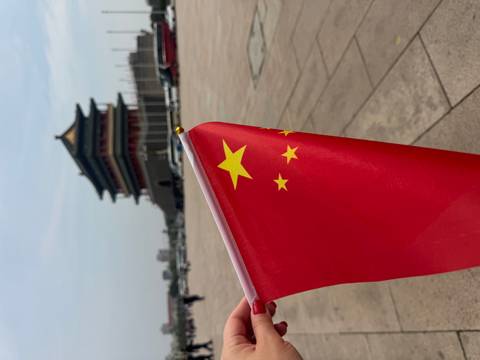       A Chinese flag held up near a traditional building.
  