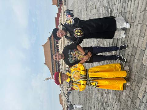       A person posing with two individuals in traditional Chinese costumes at a historic site.
  