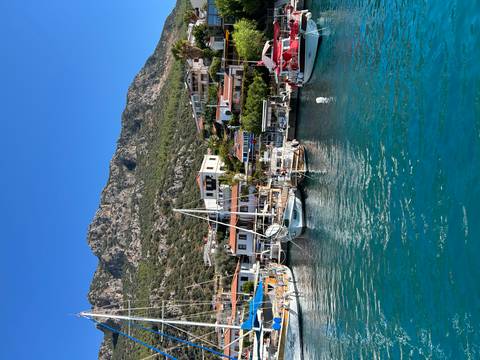       Scenic harbor with boats and village against mountainous backdrop.
  