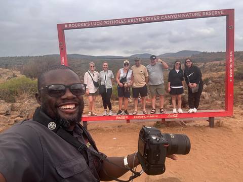 Group posing inside a large frame with scenic background.