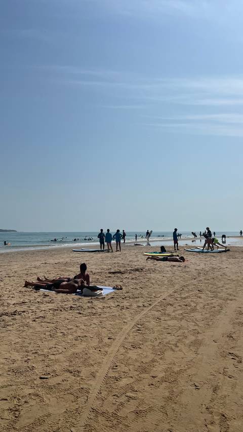 Beach with surfers and people relaxing under the sun.