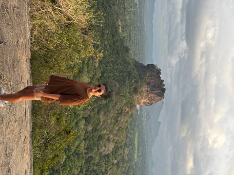       Person posing in front of Sigiriya Rock in a lush landscape.
  