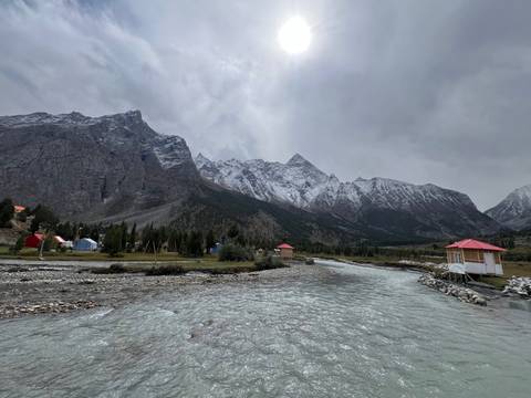 Wooden cabins near a river set against snowy mountains.