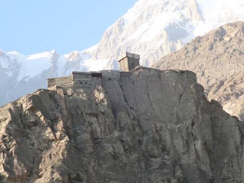 Old fortress perched atop a rugged hill with mountains.