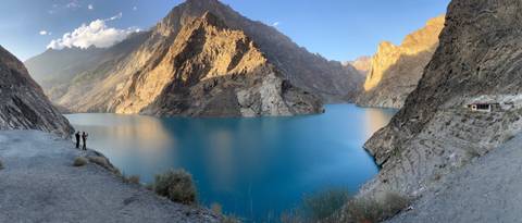 Stunning blue lake with mountainous terrain and two people admiring the view.