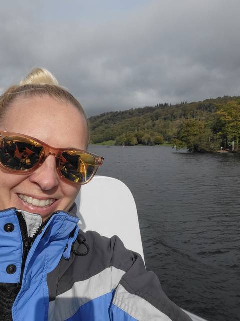 Close-up of a person on a boat with a lake and trees in the background.