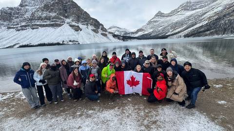 A group of people holding a Canadian flag in a snowy landscape by a lake.