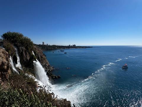       Waterfall flowing into the sea with cityscape in the distance.
  