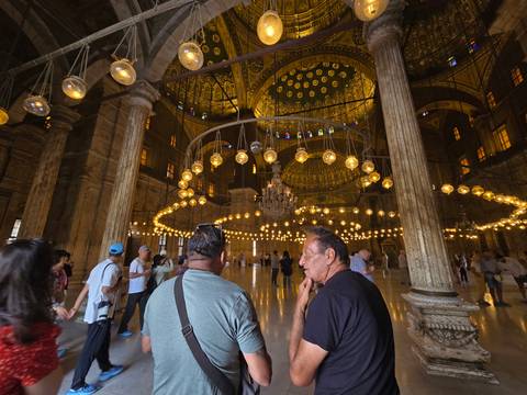 Interior of a mosque with ornate chandeliers and visitors inside.