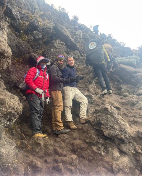 Group of hikers on a rocky path, one person climbing with assistance.