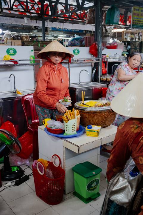 Person serving street food with condiments on a table.