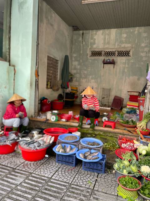 Two people sitting at a market stall with fish and vegetables