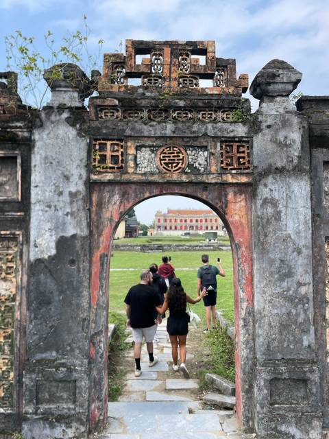       People walking under ornate stone arches in a historic site
  