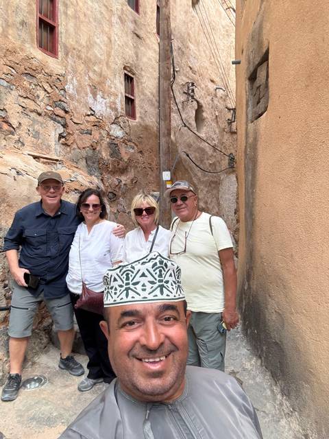       Four people standing in front of a stone building with a person wearing a decorative hat partially visible.
  