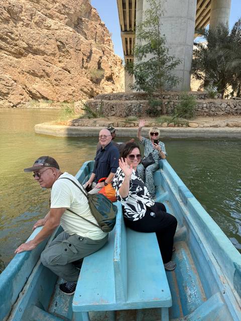      People sitting in a boat on a calm river waving at the camera.
  
