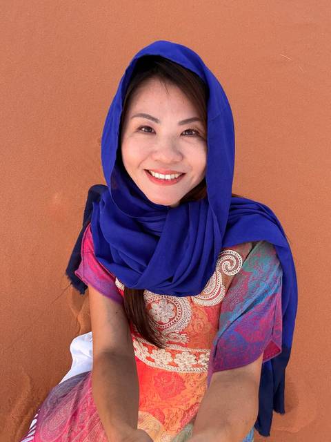       A woman wearing a blue scarf with a sandy background.
  