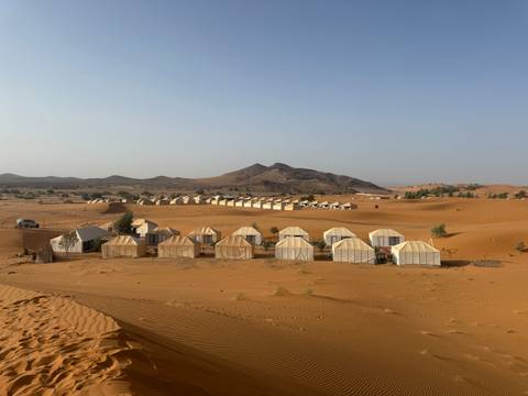 Desert campsite with groups of tents set in sandy terrain.