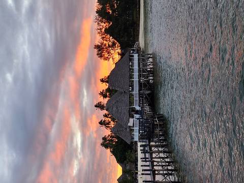 Sunset over a coastal beachfront view with a pier and huts.