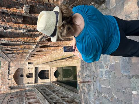A person taking a photo at an ancient stepwell with stone architecture.
