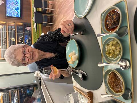       An elderly woman enjoying a meal with a glass of wine.
  