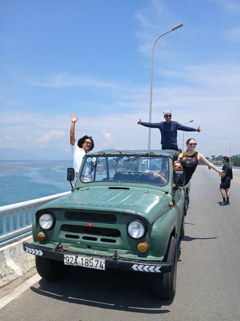 Tourists posing in an open-top car on a bridge.