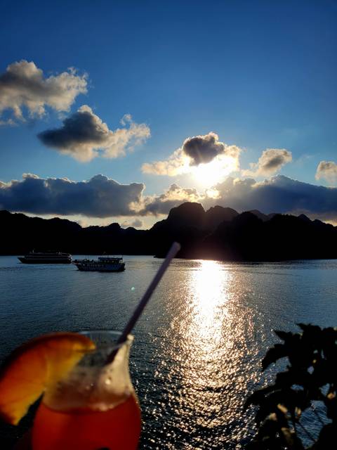 Boats floating on reflective water under dramatic sunset.