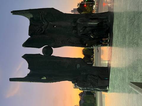 Large statue with an orb between two halves, set against sunset.