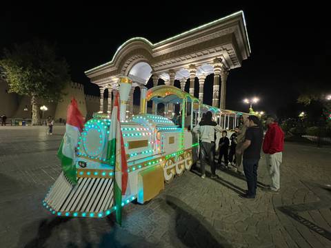       Decorative train with illuminated lights and people around it at night.
  