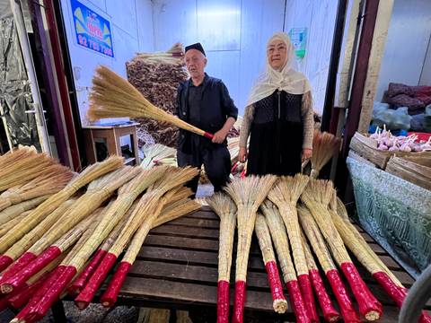       Two people selling traditional brooms in a market.
  