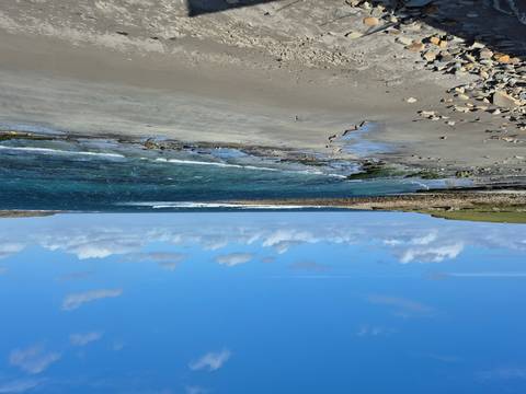       Rocky shoreline with waves under a blue sky.
  