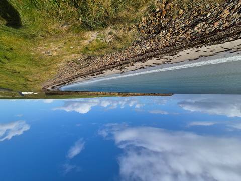       A scenic view of a beach with clear blue water and cloudy sky.
  