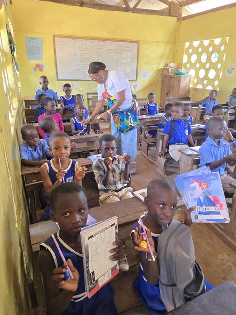 Classroom of children with a teacher handing out items.