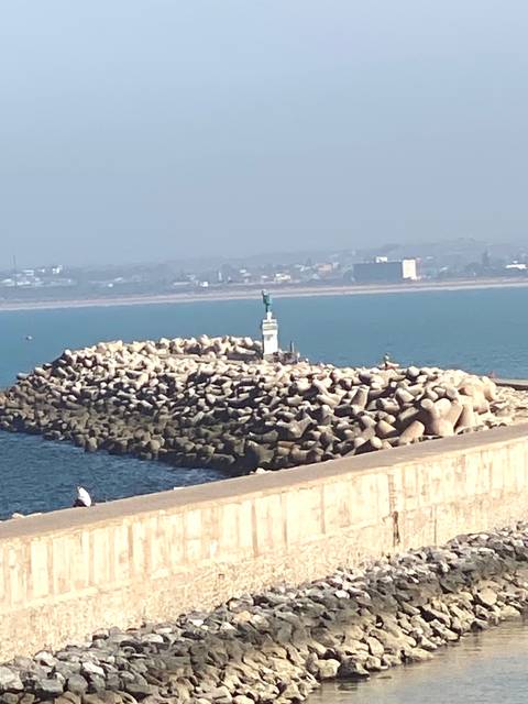 View of a breakwater and lighthouse with city skyline in the background.