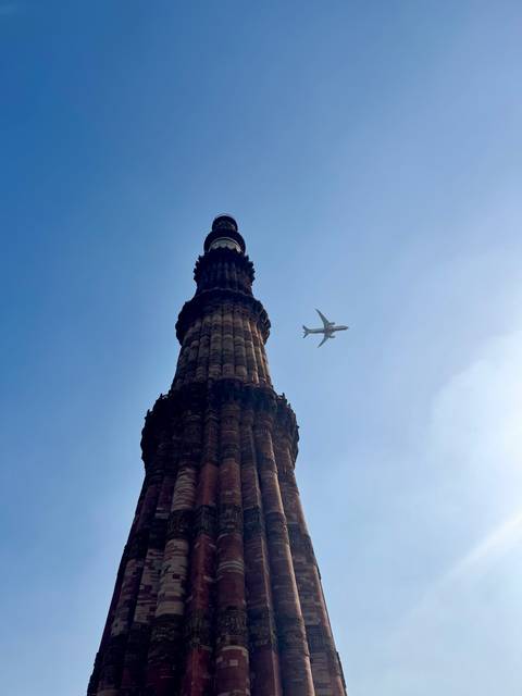 Tall stone minaret with a plane flying nearby against a clear sky.