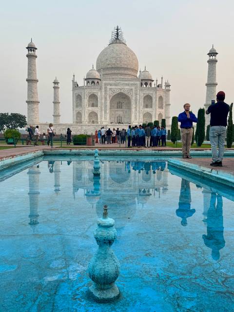 Reflection of the Taj Mahal in the pool with visitors in the background.