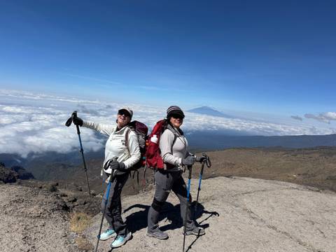       Two hikers posing on a mountain with clouds below.
  