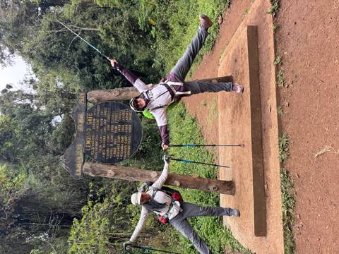 Two hikers posing by an entrance sign, smiling.