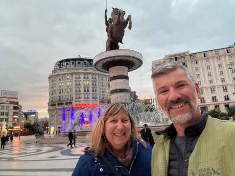 Smiling couple in front of a city fountain at sunrise or sunset.
