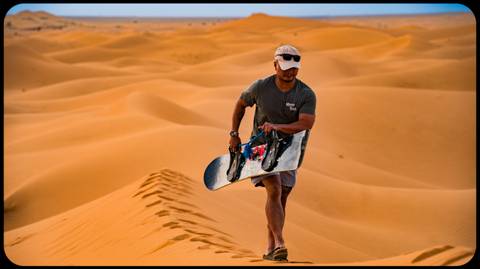 A man sandboarding in a vast desert landscape.
