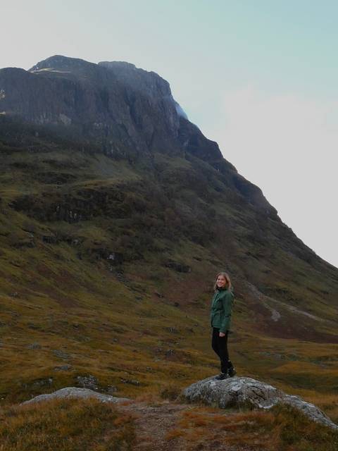 Person standing by a large rock face in a valley.