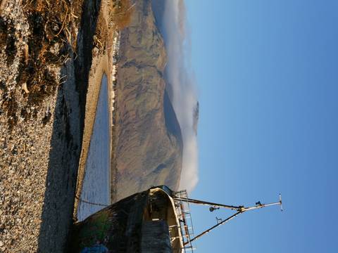 Derelict boat on a pebble beach with mountains.