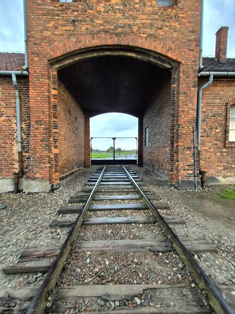Brick entrance with railway tracks leading to a gate, surrounded by red brick walls.