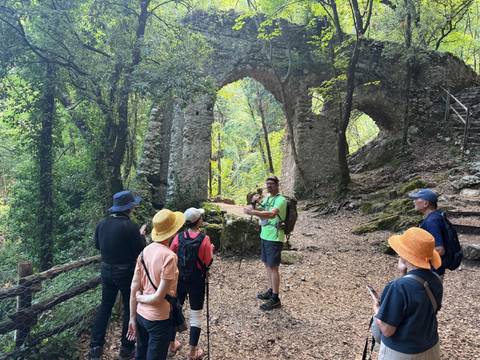 Tourist group with a guide near ancient stone archway in the forest.