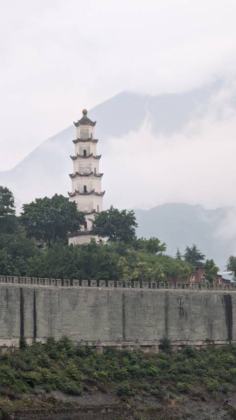 A traditional Chinese tower surrounded by trees with mountains in the background.