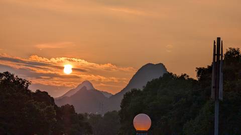       A scenic sunset with silhouetted mountains and trees.
  