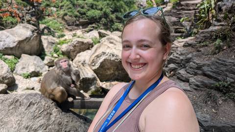 A person posing with a monkey sitting on rocks.