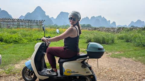       A person riding a scooter with mountains in the background.
  